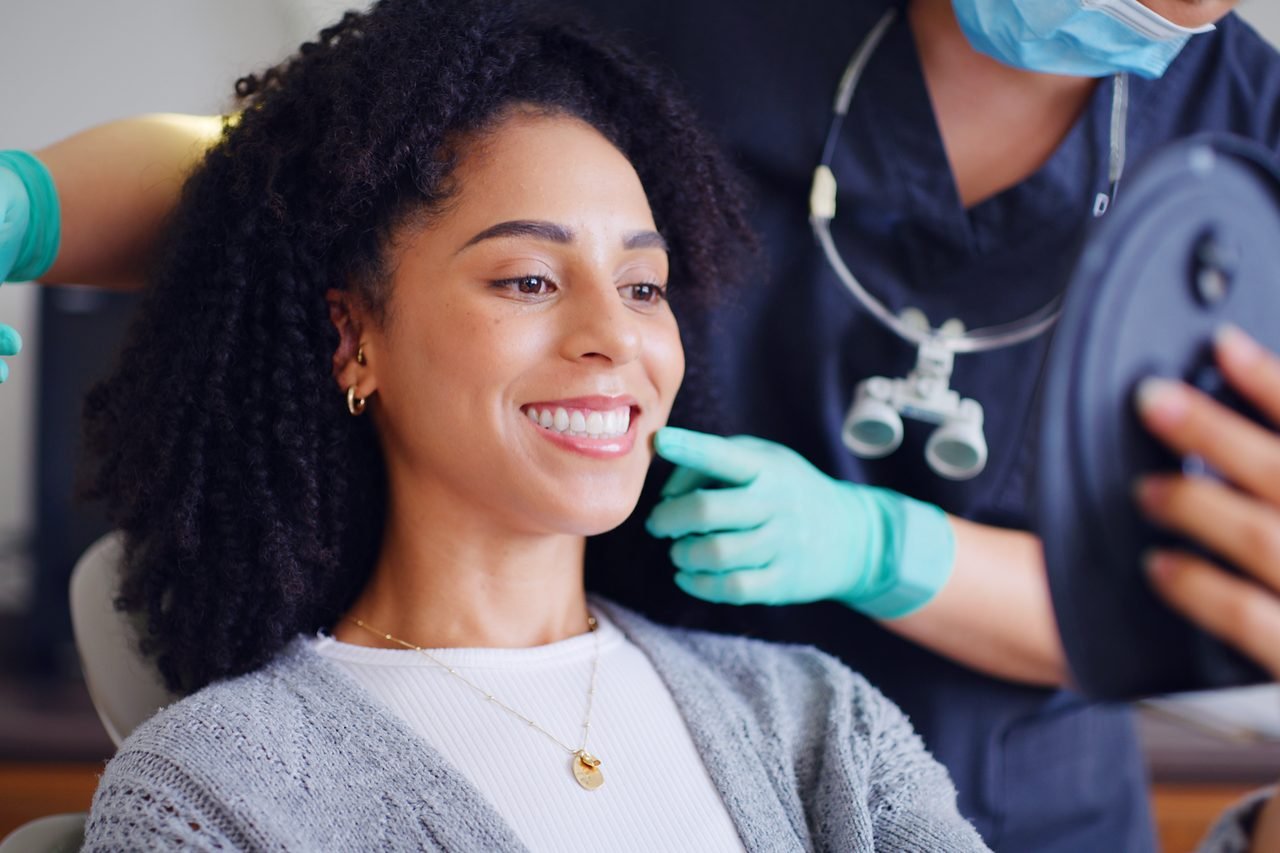 Patient checking her smile in a hand mirror while her dentist examines her teeth