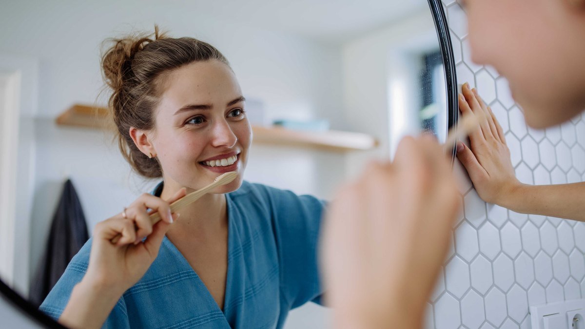 Keeping the rest of the mouth clean while an extraction site heals Patient brushing her teeth carefully in front of a bathroom mirror while recovering from a tooth extraction
