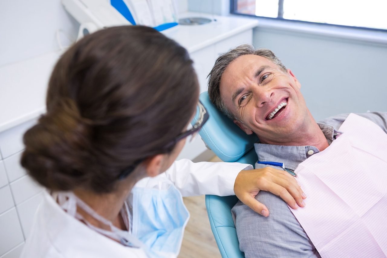 Ongoing gum care visits at University Dental Group Smiling man in the dental chair talking with his dentist during a checkup