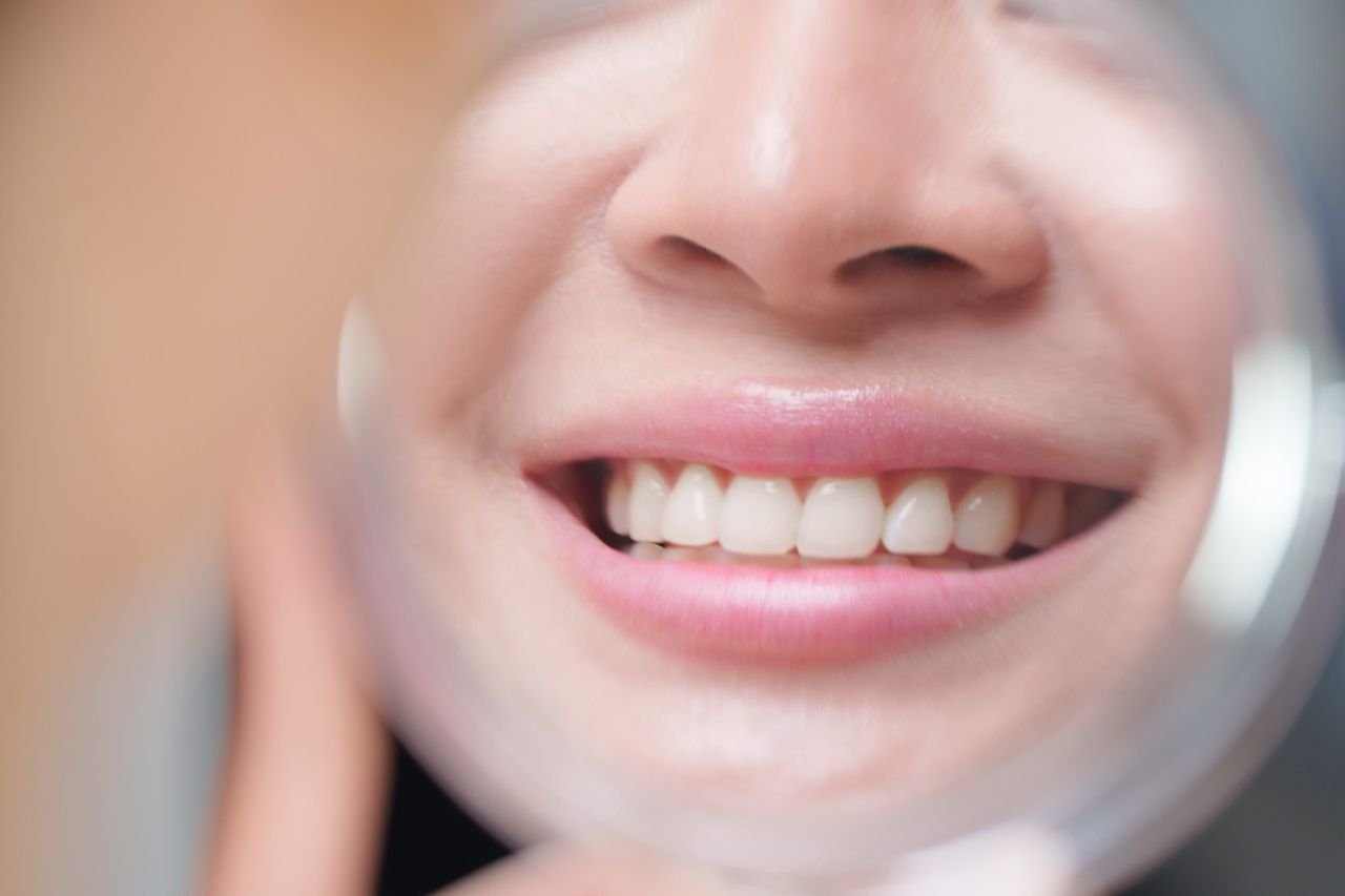 Plaque can be brushed away; tartar needs a cleaning Close-up of a smiling patient checking their teeth in a hand mirror