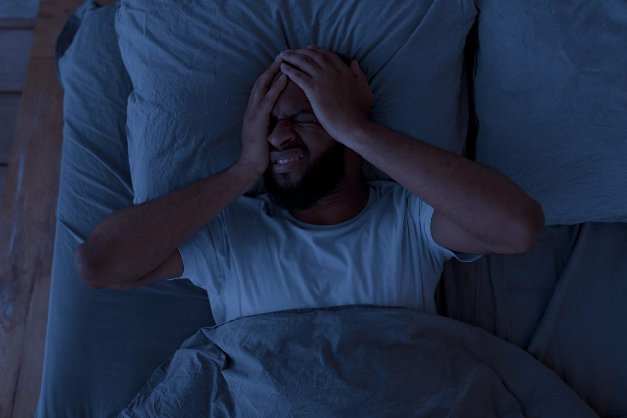 Man lying awake in bed at night pressing his hands to his head